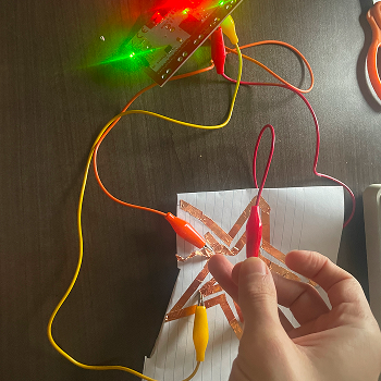 Bridging the two copper tape paths with a finger to complete the circuit between them, testing the body as a conductor between two separate conductive surfaces.