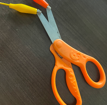 Connecting a pair of scissors to a single alligator clip to test conductivity, the metal blades successfully complete the circuit when touched, triggering a keypress.